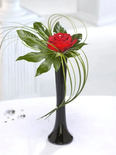 Single Red Rose - Simple elegance. A single red Rose with a twinkle of Diamante in an elegant black vase. The perfect way to say "I love You" to that someone special. Contains: 1 Red Rose, Aralia Leaf, Steel Grass, Black Lily Vase & Diamante Pins
